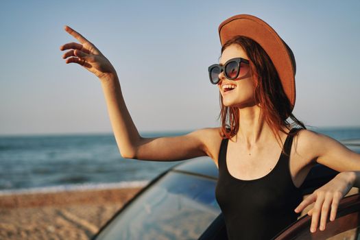 cheerful woman in sunglasses and a hat on the ocean near the car. High quality photo