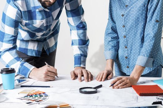 Man carefully studying technical drawing with magnifying glass. Designers working with color swatches and construction blueprint at workplace. Thorough analysis and inspection of design project.