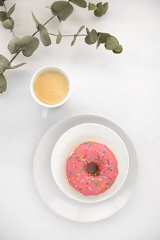 From above shot of delicate branch of houseplant lying near cup of fresh coffee and yummy doughnut on white background