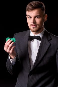 man in a suit posing with chips for gambling on black background