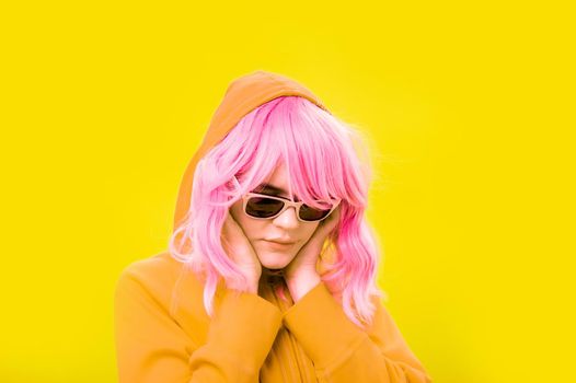 Alternative funky girl with pink hair on yellow background. Close up fashion portrait young beautiful woman in hoodie and glasses. Unusual youth fashion concept. Hot image.