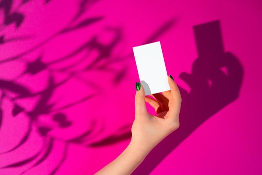 Female hand holding blank businesscard. Creative photo with shadow close up