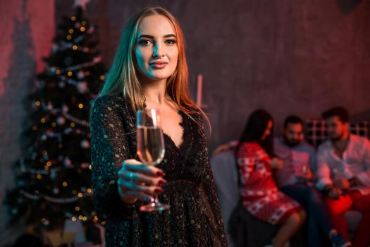 Beautiful young woman with glass of champagne at Christmas party. Funny people.