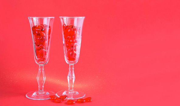 Two champagne glasses are filled with glass hearts on a red background with space for text. Valentine's Day, love, romantic date