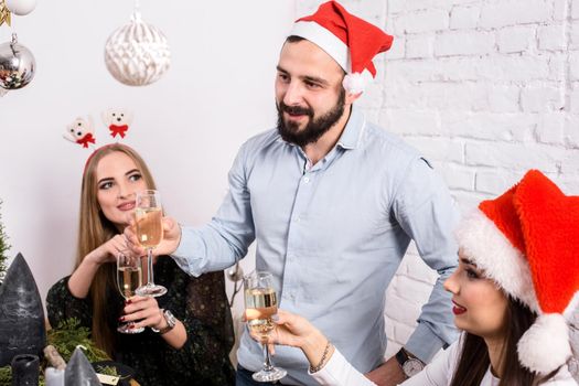 Christmas party cheerful friends at having drink and fun. Men and women at a festive table with glasses of champagne in a white room