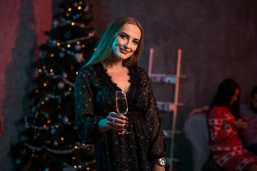 Beautiful young woman with glass of champagne at Christmas party. Funny people.