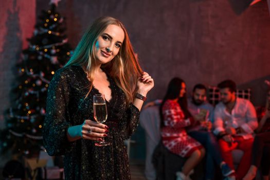 Beautiful young woman with glass of champagne at Christmas party. Funny people.