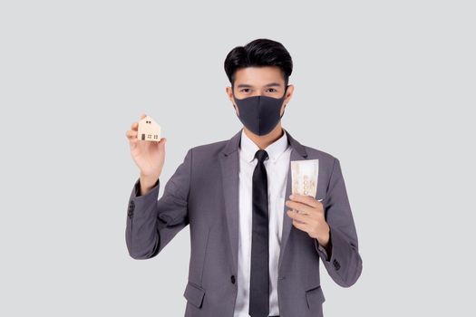 Young asian businessman in face mask holding money Thai and home isolated on white background, pandemic and crisis of economic, business man and investment property during disease covid-19.