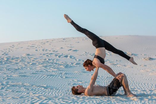 Couple of young sporty people practicing yoga lesson with partner, man and woman in yogi exercise, arm balance pose, working out, indoor full length. Yoga practice on the sand