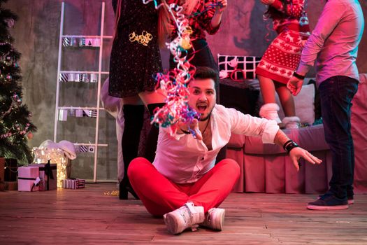 Friends celebrating Christmas or New Year eve at home. A young man sits on the floor in the foreground the rest stand behind him and have fun.