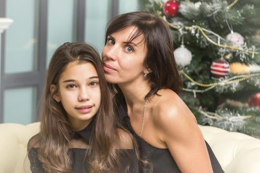 Happy mother and daughter near the Christmas tree are sitting on the couch. Family holidays concept.