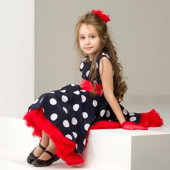 Beautiful Girl Wearing Polka Dot Dress and Black Shoes Sitting on White Stairs and Smiling at Camera, Full Length Portrait of Charming Coquettish Girl Posing in Retro Fashion Dress in Studio