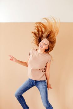 Full length portrait of a joyful young woman jumping and celebrating over cream background