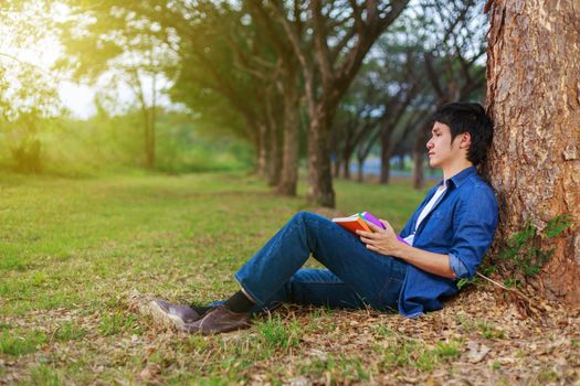 young man sitting and holding a book in the park