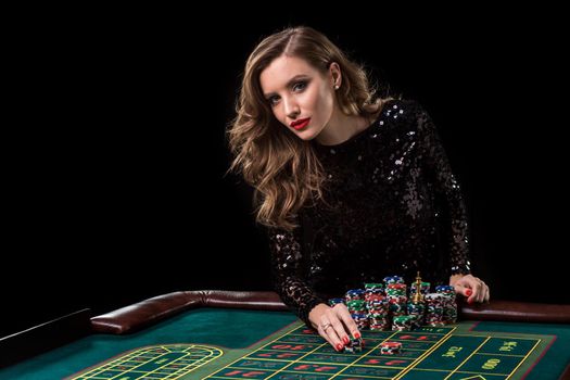Sexy woman in a black dress playing in casino. Woman stakes piles of chips playing roulette at the casino club. Gambling. Roulette.