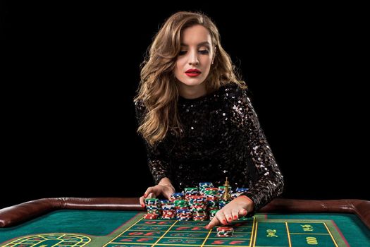 Sexy woman in a black dress playing in casino. Woman stakes piles of chips playing roulette at the casino club. Gambling. Roulette.