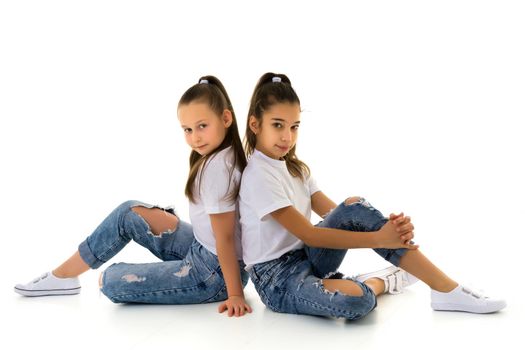 Two cute little girls are sitting on the floor in a studio on a white background. Concepts of style and fashion, happy childhood. Isolated.