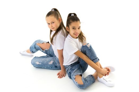 Two cute little girls are sitting on the floor in a studio on a white background. Concepts of style and fashion, happy childhood. Isolated.