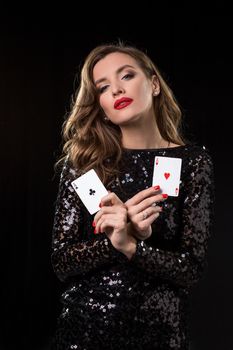 Young beautiful woman in black shiny dress holds poker cards in hands against a black background. The concept of gambling. Casino