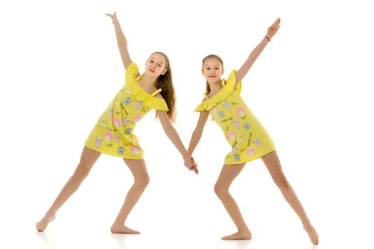 Cute Teen Girls Standing Together and Holding Hands, Two Barefoot Sisters Wearing Yellow Short Summer Dresses Smiling at Camera, Full Length Portrait of Cheerful Teenagers Isolated on White Background.