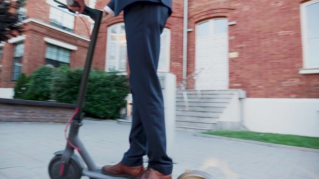 Diplomatic man in business suit riding on electric scooter to company office. Entrepreneur using contemporary ecological transport to go on business meeting. Concept of eco-friendly transportation