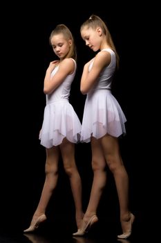Two charming gymnasts in beautiful sports swimsuits posing in the studio. The concept of children's sports, fitness. Isolated on a black background.