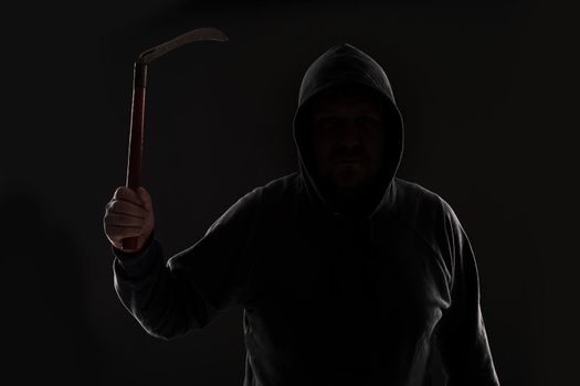 Criminal in dark clothes and balaclava with scythe. On black background at the studio. Bandit and thief