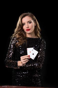 Young beautiful woman in black shiny dress holds poker cards in hands against a black background. The concept of gambling. Casino