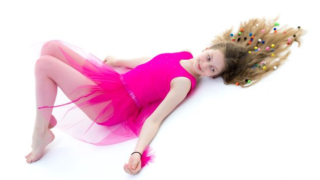 Beautiful girl gymnast schoolgirl lying on the floor with long hair spread out on the floor, in which multicolored confetti are braided. The concept of sport, style and fashion. Isolated on white background.