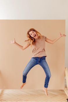 Full length portrait of a joyful young woman jumping and celebrating over cream background