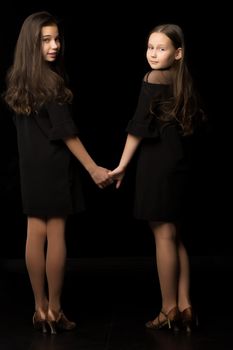 Two cute little girls are holding hands. Studio photography on a black background.