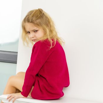 Beautiful Girl Sitting on White Cube and Gesturing, Smiling Adorable Blonde Girl Wearing Red Knitted Dress and Sneakers Posing at the Camera, Portrait of Cheerful Preschooler Child