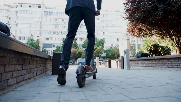 Businessman in diplomatic suit riding on electric scooter going to company office. Entrepreneur uses contemporary ecological transport to go on business meeting. Concept of eco-friendly transportation