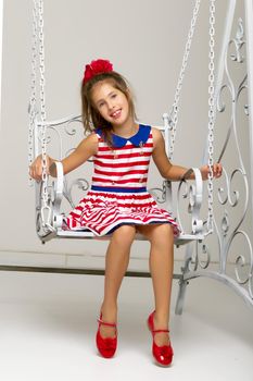 Beautiful little girl swinging in the studio on a swing. Concept of a happy childhood, family well-being.