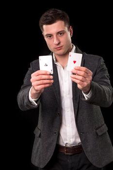 Young caucasian man in a dark suit and a white shirt holding two aces in his hands on black background. Gambling concept. Casino