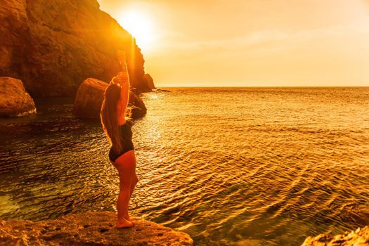 Young woman in swimsuit with long hair practicing stretching outdoors on yoga mat by the sea on a sunny day. Women's yoga fitness pilates routine. Healthy lifestyle, harmony and meditation concept.