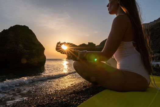 Young woman in swimsuit with long hair practicing stretching outdoors on yoga mat by the sea on a sunny day. Women's yoga fitness pilates routine. Healthy lifestyle, harmony and meditation concept.