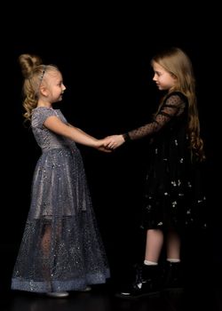 Two cute little girls are holding hands. Studio photography on a black background.