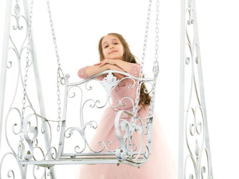 Beautiful girl standing next to an elegant metal swing on a white background, portrait of a beautiful girl in a magnificent dress, seriously looking at the camera