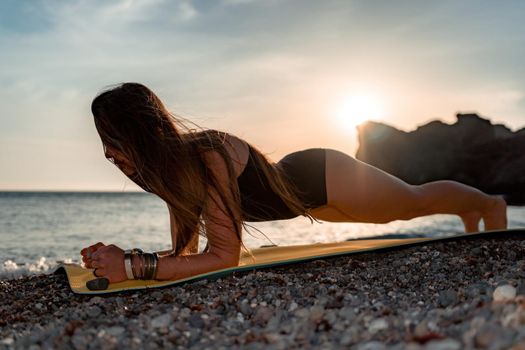 Young woman in swimsuit with long hair practicing stretching outdoors on yoga mat by the sea on a sunny day. Women's yoga fitness pilates routine. Healthy lifestyle, harmony and meditation concept.