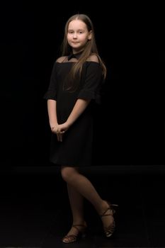 Cute little girl in a beautiful dress on a black background. Studio photo.