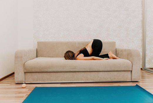Young woman with long hair, fitness instructor in black sportswear, doing stretching and pilates on yoga mat at home. Female fitness yoga routine concept. Healthy lifestyle harmony and meditation