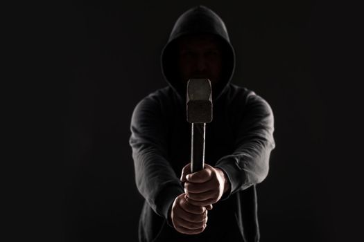 Criminal in dark clothes and balaclava with hammer. On black background at the studio. Bandit and thief