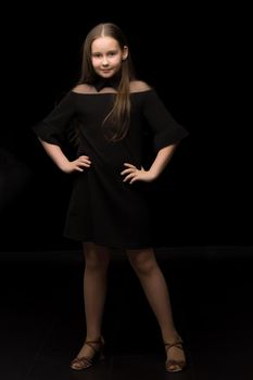 Cute little girl in a beautiful dress on a black background. Studio photo.