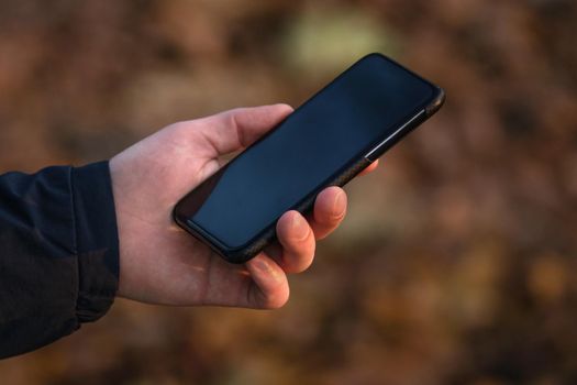 Male hand holding a mobile phone with black screen mockup. Template for web design or app presentation. Gadget closeup. Space for text. Concept of digitalization, business, remote work and freelance