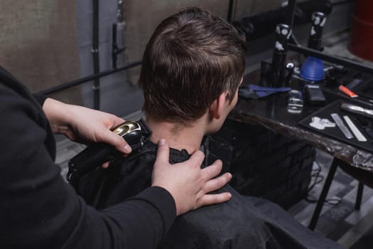 Barber or hairdresser cuts the back of the head of a guy with dark hair with a machine. Hairdressing.