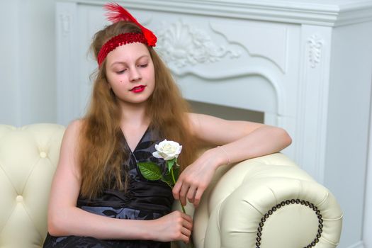 Very beautiful teen girl sitting on a couch holding a flower in her hand. The concept of style and fashion.