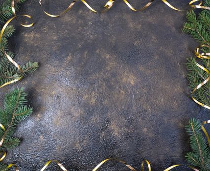 Christmas composition of fir branches and a gold ribbon in the form of a frame with a place for text on a black oil with gold embossing background.