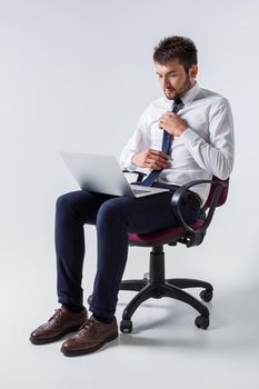 emotional young guy in office clothes working on a laptop computer and sitting on a chair. corrects tie