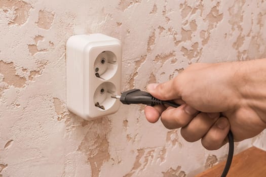 A man hand inserts or removes a plug from an outlet in a modern interior. Safe use of electrical appliances concept.